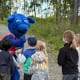 A group of children are standing around a blue mascot