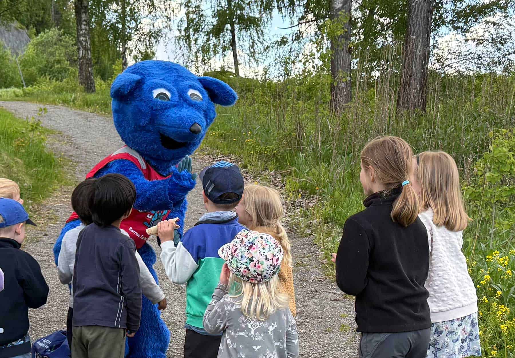 A group of children are standing around a blue mascot
